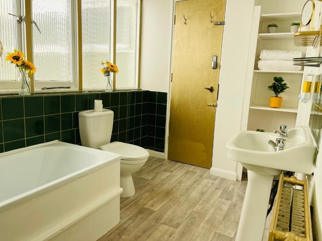 Un baño con bañera, inodoro y lavamanos. Hay plantas en macetas y un espejo sobre el lavamanos.