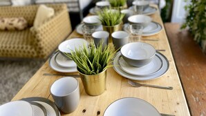 Ein Holzespeisetisch, gedeckt mit Tellern, Schüsseln und Tassen, mit kleinen Topfpflanzen in der Mitte.