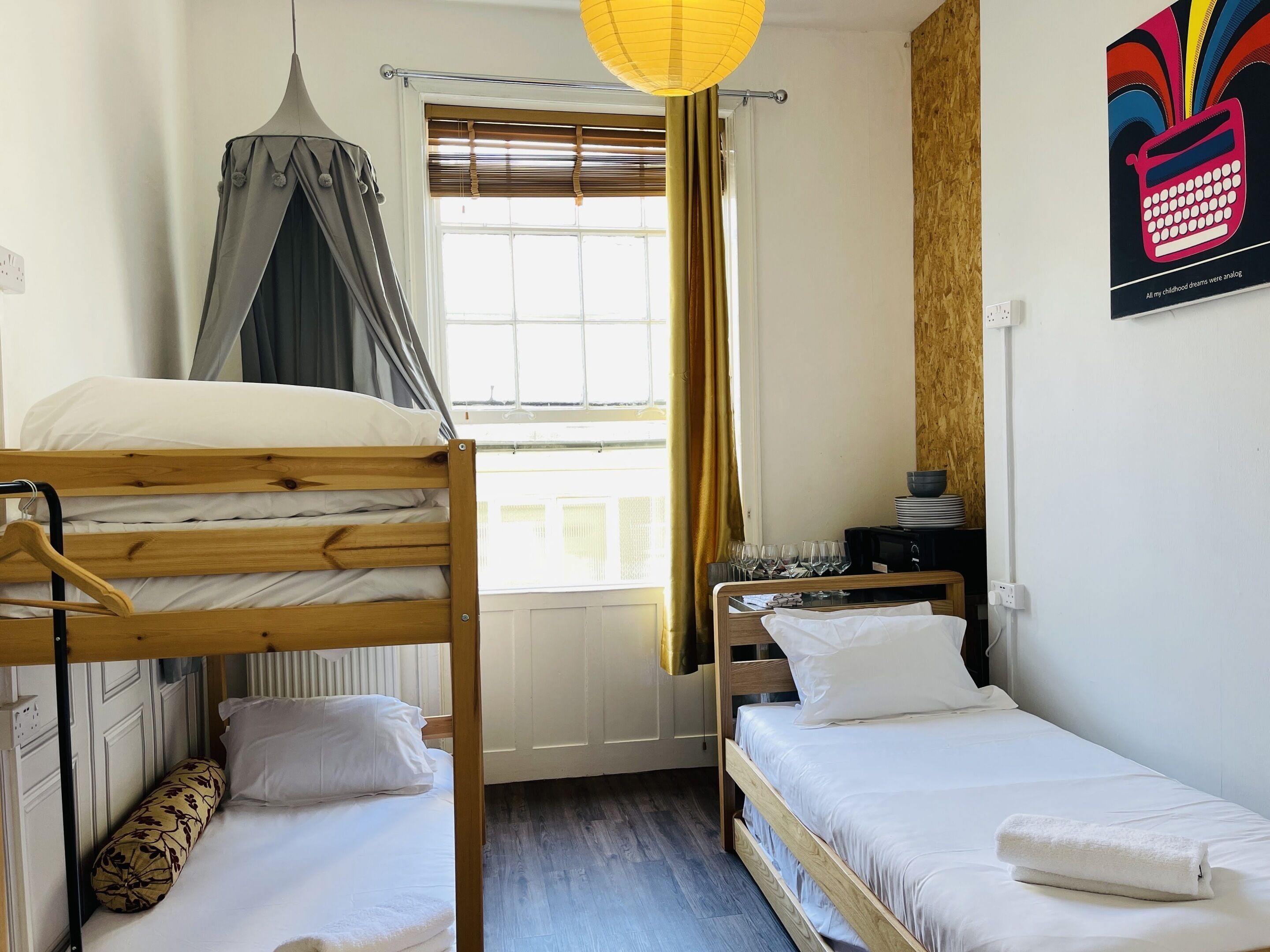 Una camera del dormitorio con letti a castello, una finestra con tende, un comodino con bicchieri e un poster appeso al muro.