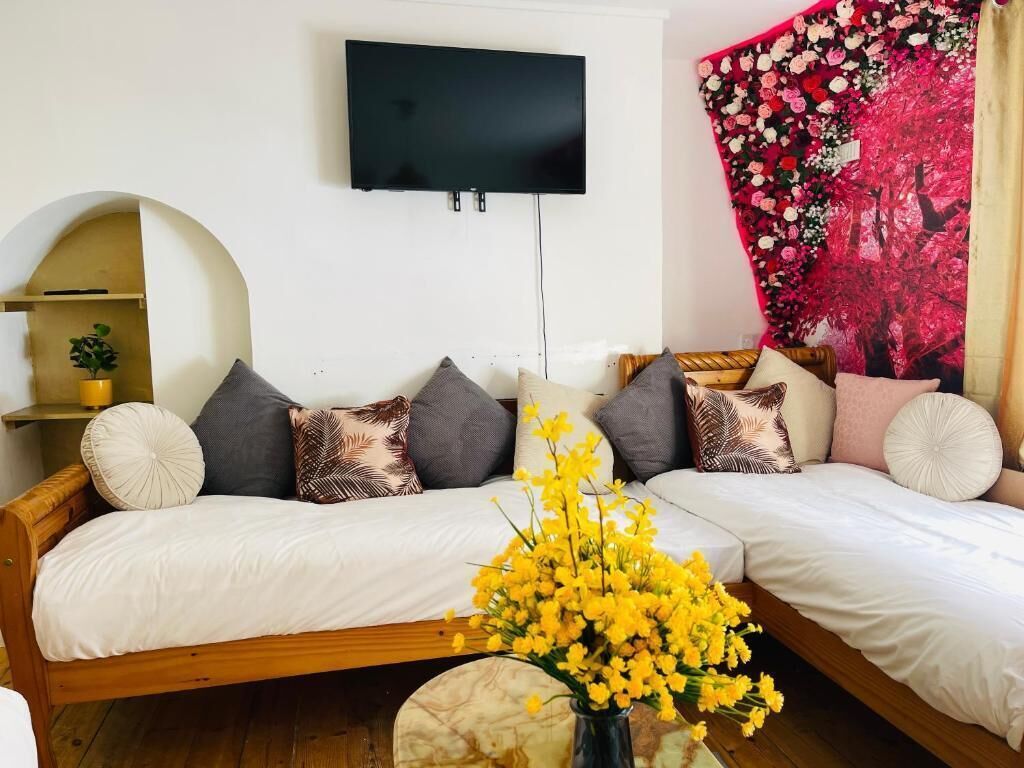 Un salon moderne avec un ensemble de canapés, un téléviseur à écran plat fixé au mur et une tapisserie florale aux couleurs vives.