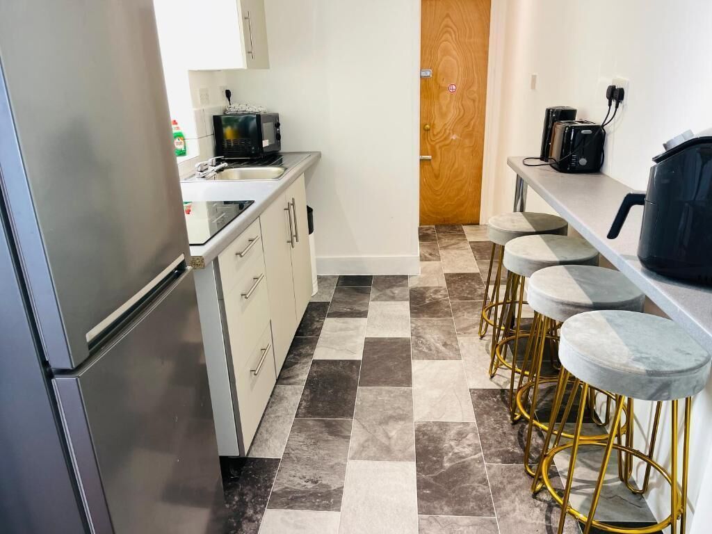 Cocina compacta equipada con refrigerador, microondas y cafetera. Hay tres taburetes en la barra.