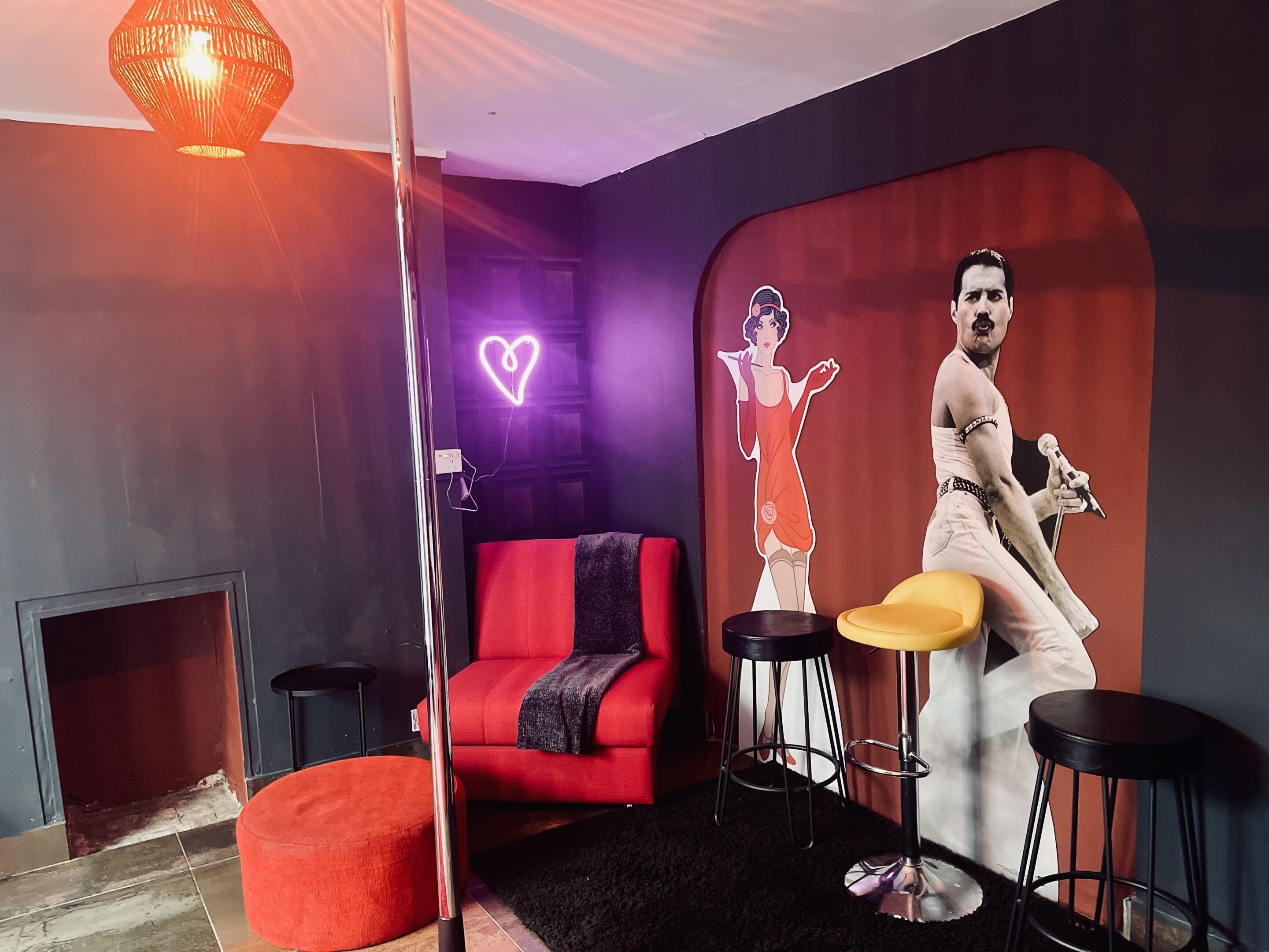 Una sala de estar moderna con un sofá rojo, taburetes negros y amarillos, una chimenea y un mural grande en la pared.