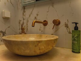 Un baño con lavamanos de mármol, grifo dorado y botella verde de champú y acondicionador.