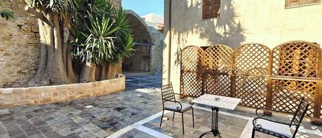A courtyard with stone flooring, a table and chairs, a wooden fence, and a building with a window.