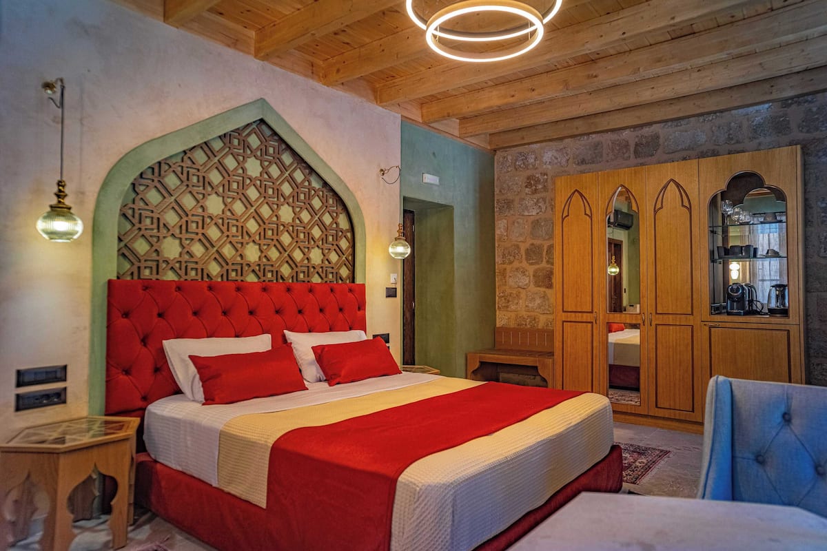 A bedroom with a red upholstered headboard, a wooden wardrobe, and a stone wall.