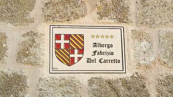 Mural de pedra com um candeeiro preto e um sinal com um brasão e o nome 'Alberto Fabrizio Del Carretto'.