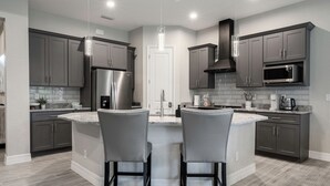 Una cocina moderna con gabinetes grises, electrodomésticos de acero inoxidable y una isla central con dos taburetes de bar.