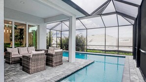 Un área de piscina interior moderna con techo de vidrio, mobiliario de mimbre y vistas del paisaje circundante.