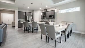Una cocina moderna con armarios grises, un comedor con mesa blanca y sillas grises, y un ventanal que proporciona luz natural.