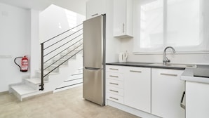 A modern kitchen with white cabinets, a stainless steel refrigerator, a black countertop, a stainless steel sink, and a staircase with a black railing. - Holiday Home 'Casa Tita Mercedes' with Private Pool, Wi-Fi and Air Conditioning (Nerja)
