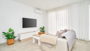 A modern living room with a sofa, a coffee table, a flat-screen TV, and two potted plants. - Holiday Home 'Casa Tita Mercedes' with Private Pool, Wi-Fi and Air Conditioning (Nerja)