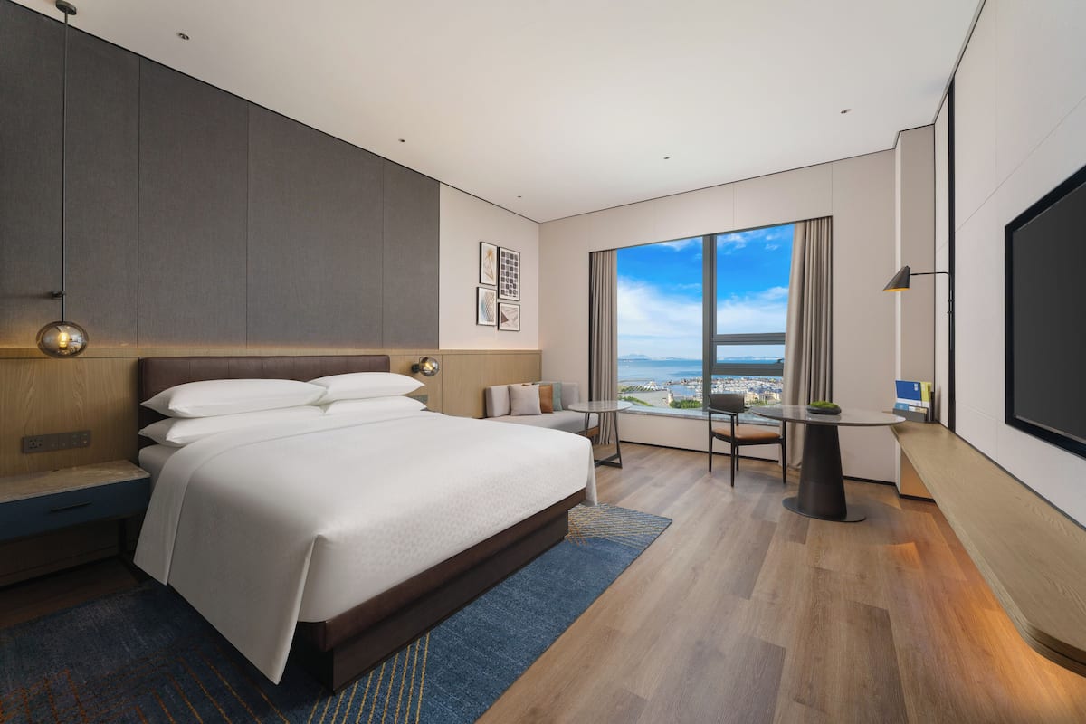 A modern hotel room with a large bed, a seating area with a view, and a flat-screen TV.