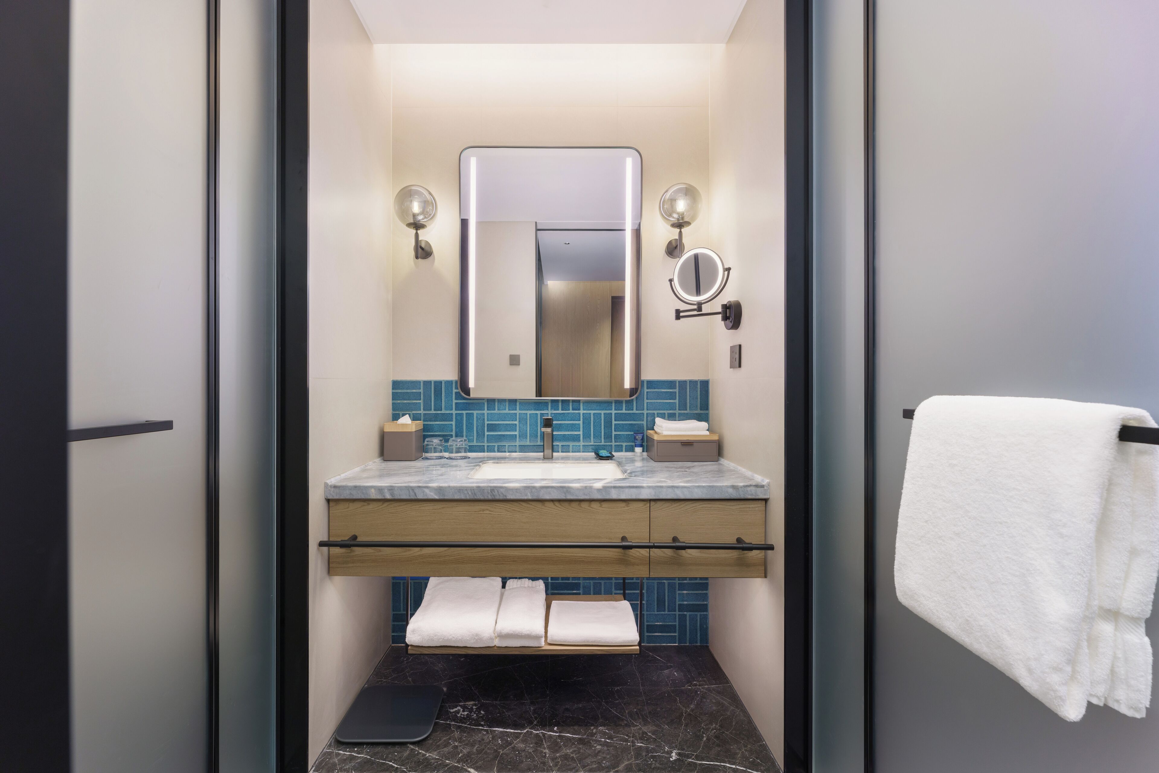 A modern bathroom with a marble sink, a large mirror, and a towel rack.