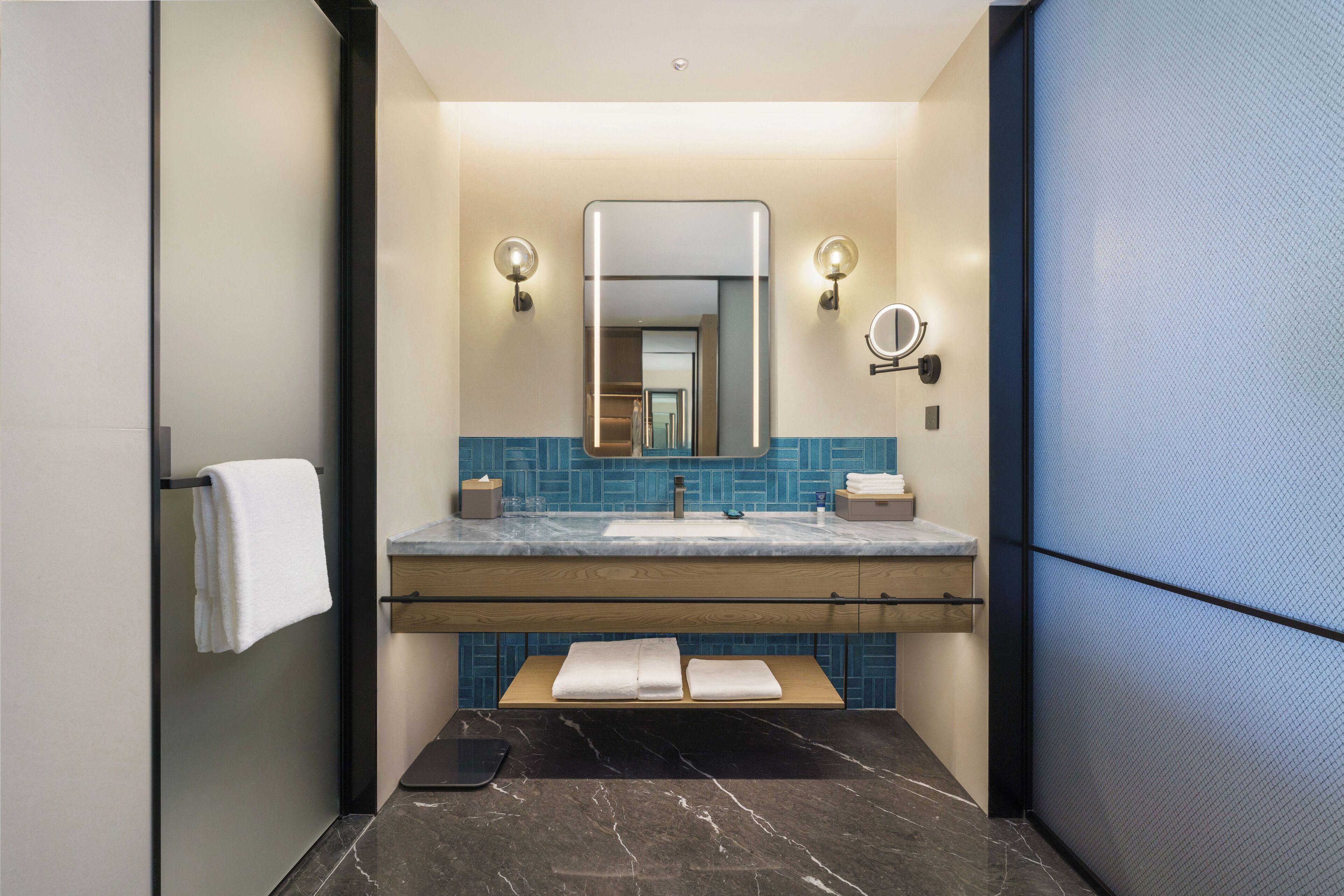 A modern bathroom with a marble sink, a large mirror, and a towel rack.