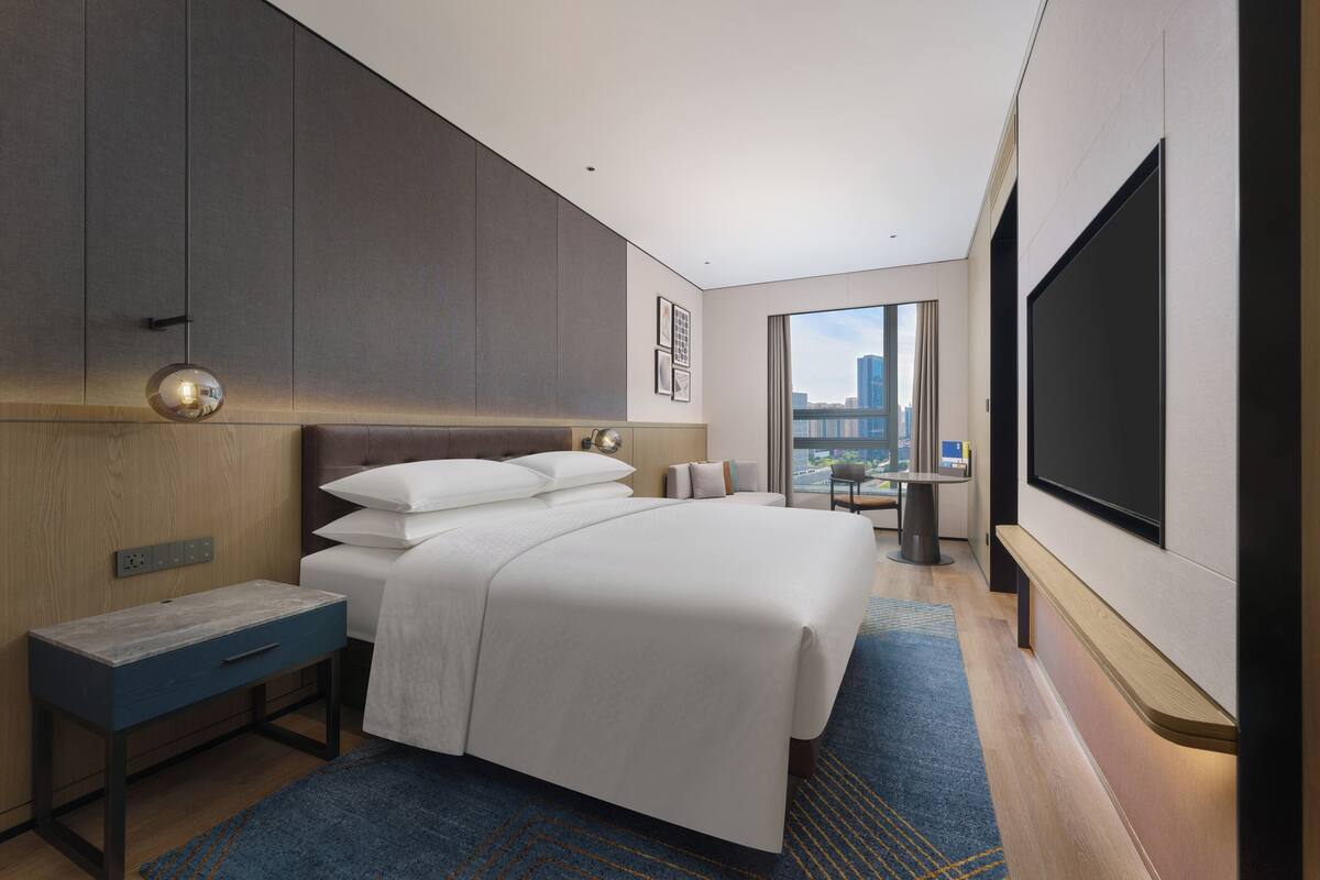A modern hotel room with a large bed, a desk, a TV, and a city view.