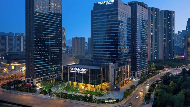 Un hotel moderno con fachada de vidrio, llamado 'Four Points by Sheraton', rodeado de edificios altos y una calle concurrida.