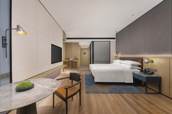 A modern hotel room with a bed, desk, chair, and a TV on the wall.