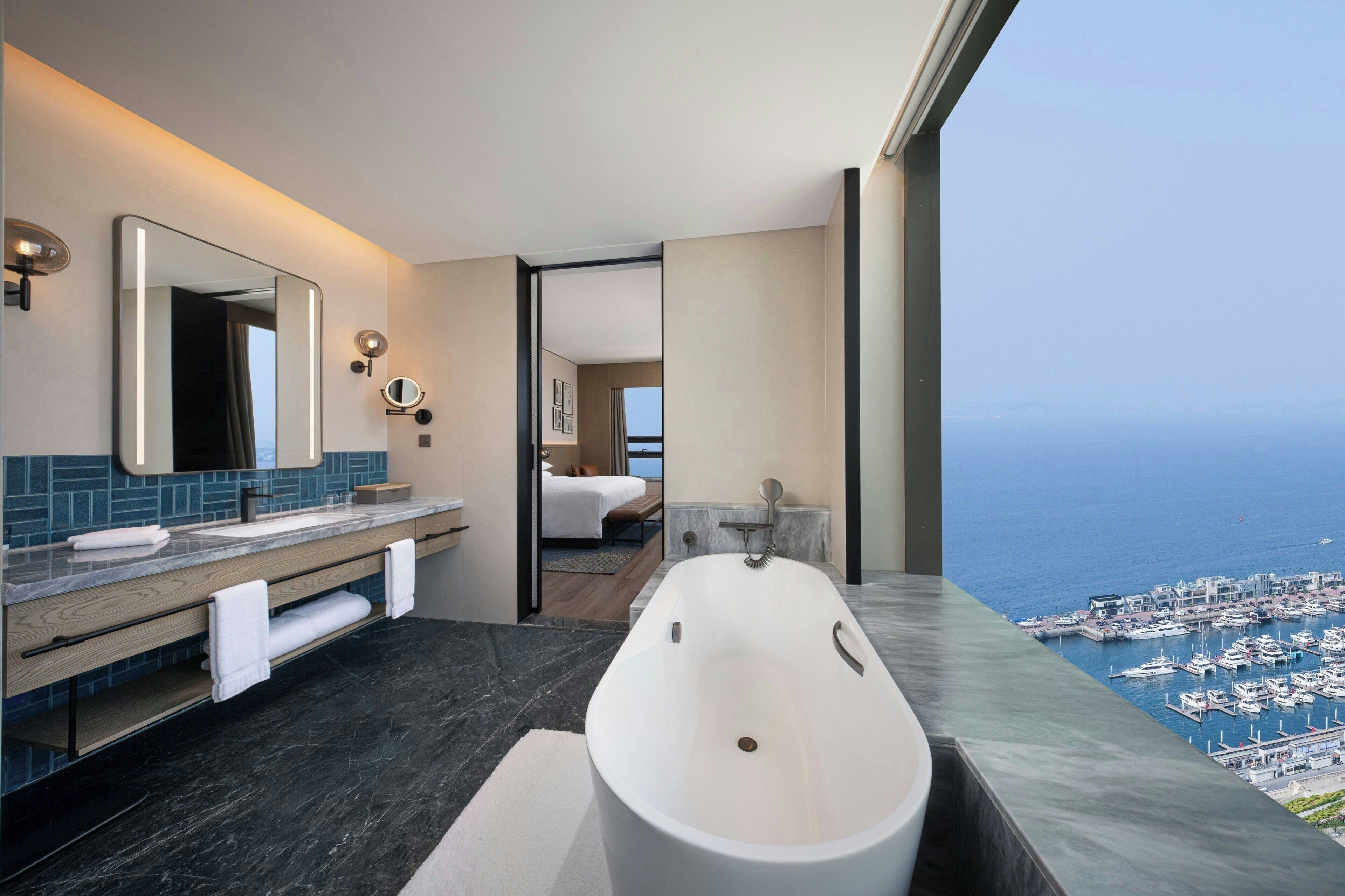 A modern bathroom with a large bathtub, a vanity with a mirror, and a view of the marina.
