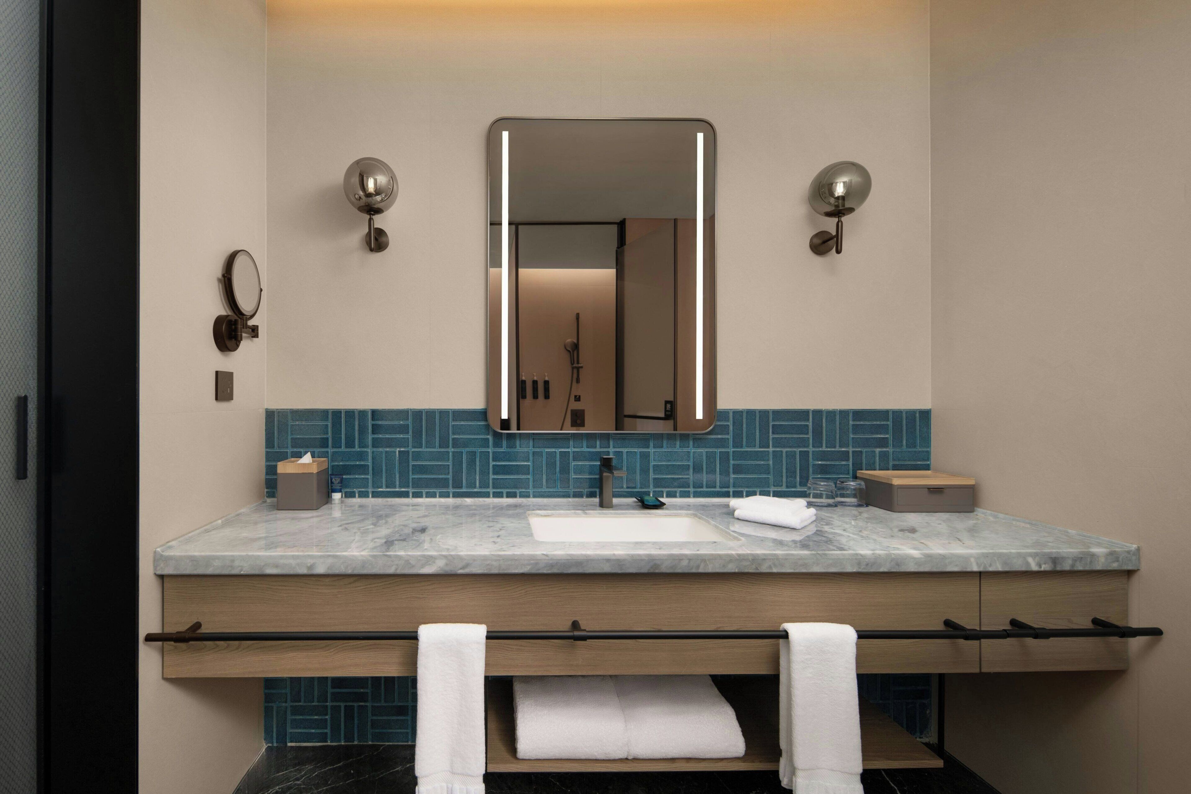 Un baño moderno con lavamanos de mármol, tocador de madera y salpicadero de azulejos azules.