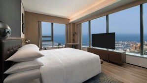 Una habitación de hotel moderna con una cama grande, un televisor de pantalla plana y vistas a la ciudad a través de amplias ventanas.