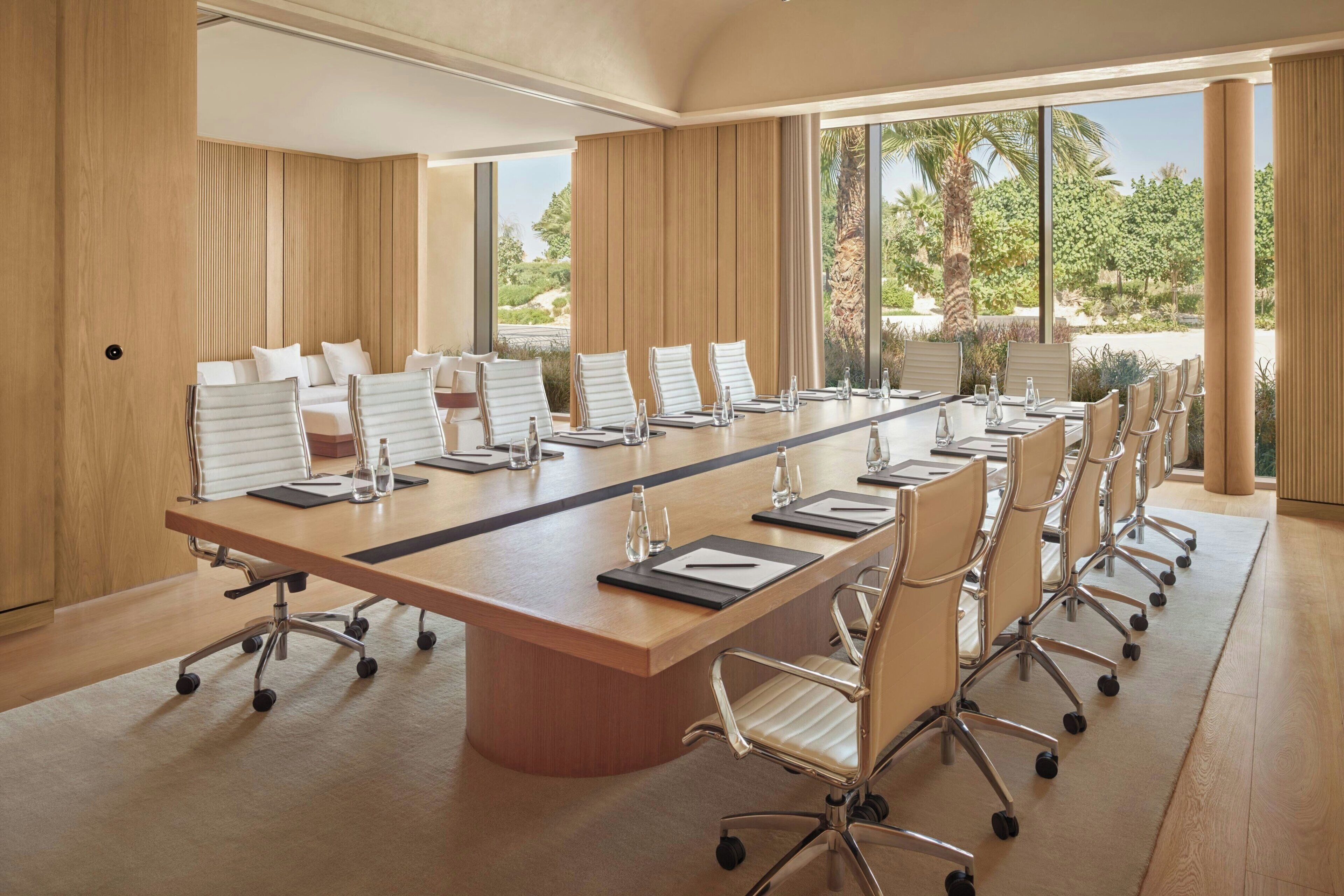 A conference room with a long table, chairs, and a view of greenery outside.