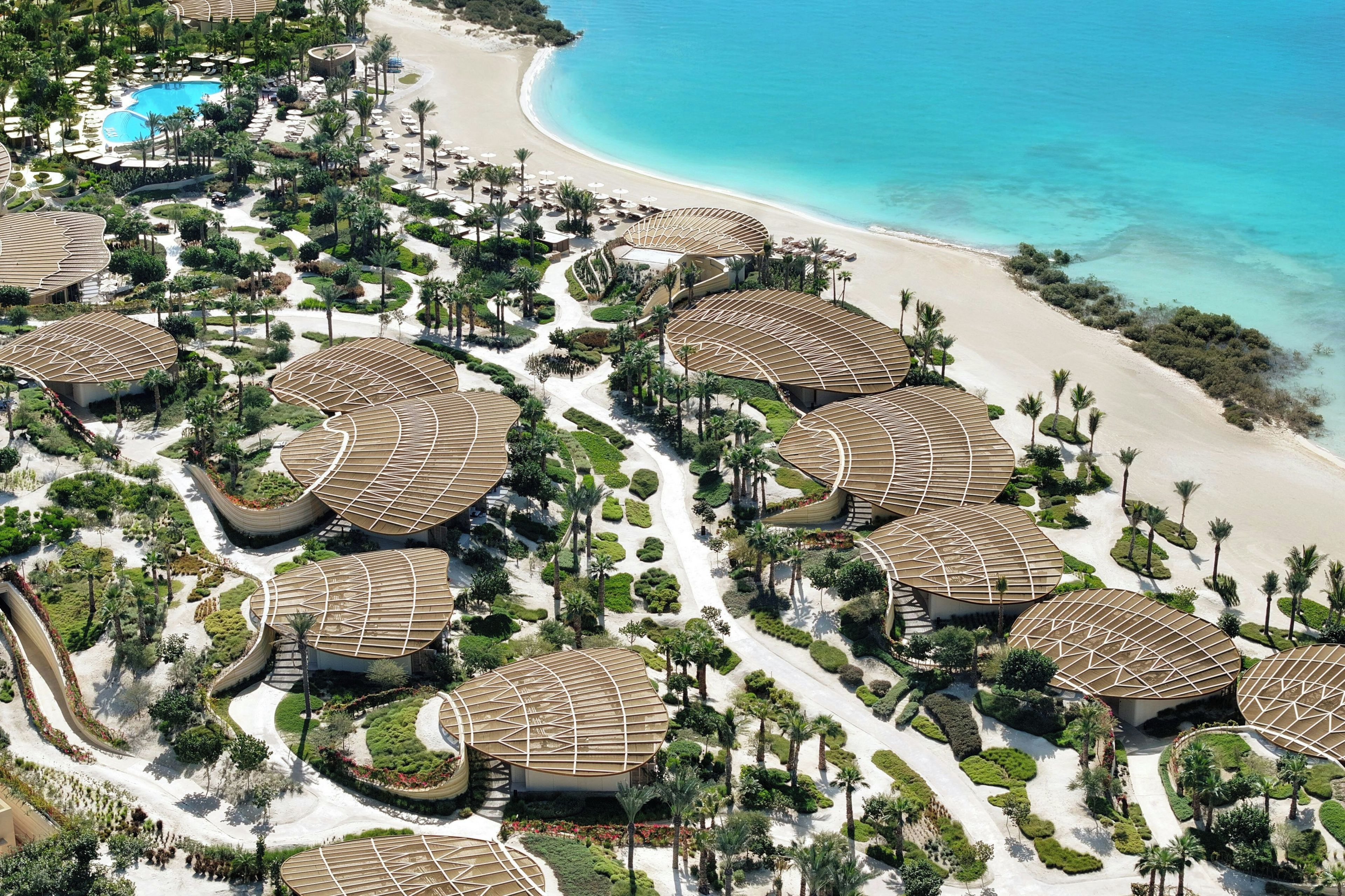 An aerial view of a resort with multiple circular-roofed buildings, a beach, and a pool.