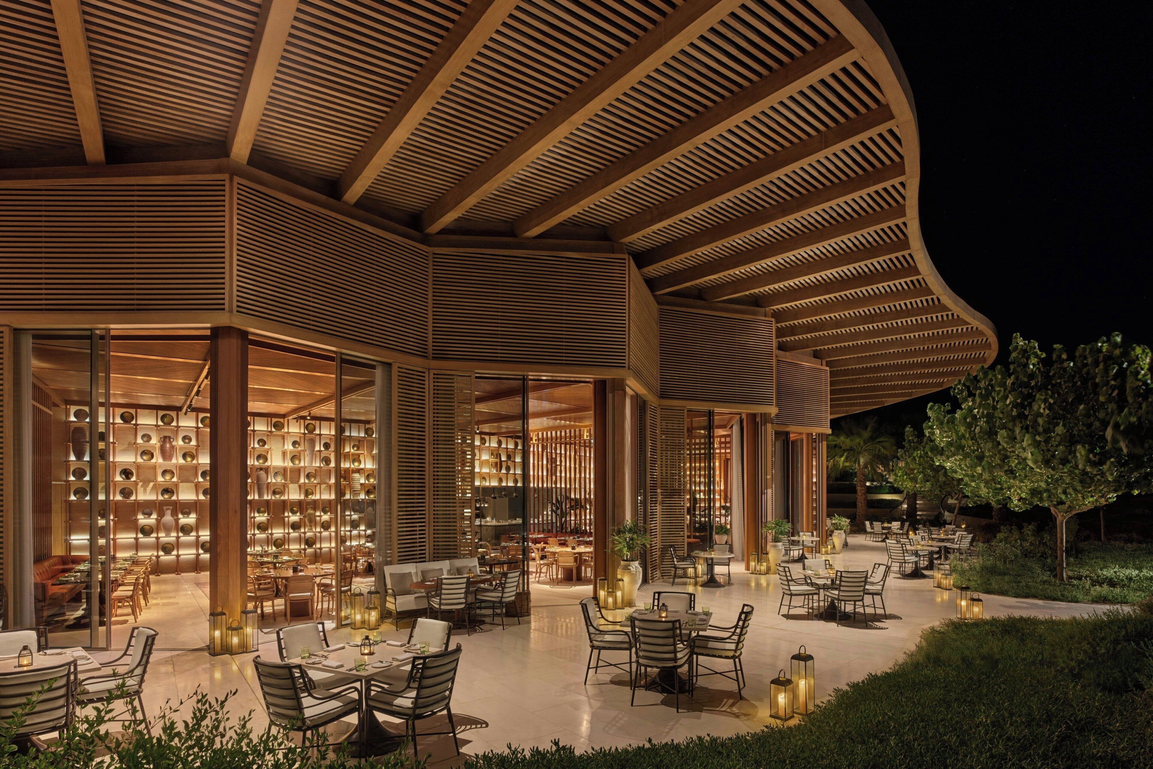 A modern outdoor dining area with tables and chairs, surrounded by a wooden structure with slatted roof design.