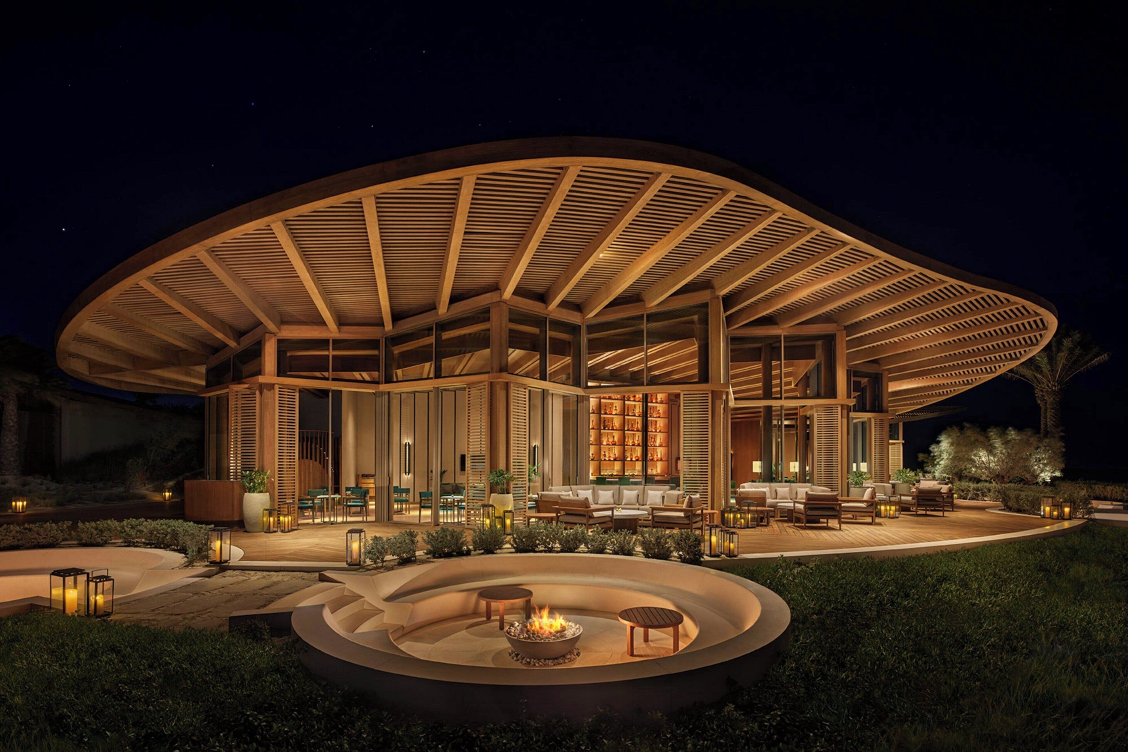 A modern, circular building with a covered patio area, outdoor seating, and a fire pit.