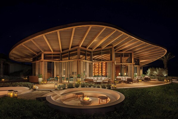 Un bâtiment moderne de forme circulaire, doté d’un patio couvert, d’un espace extérieur aménagé pour s’asseoir et d’un foyer.