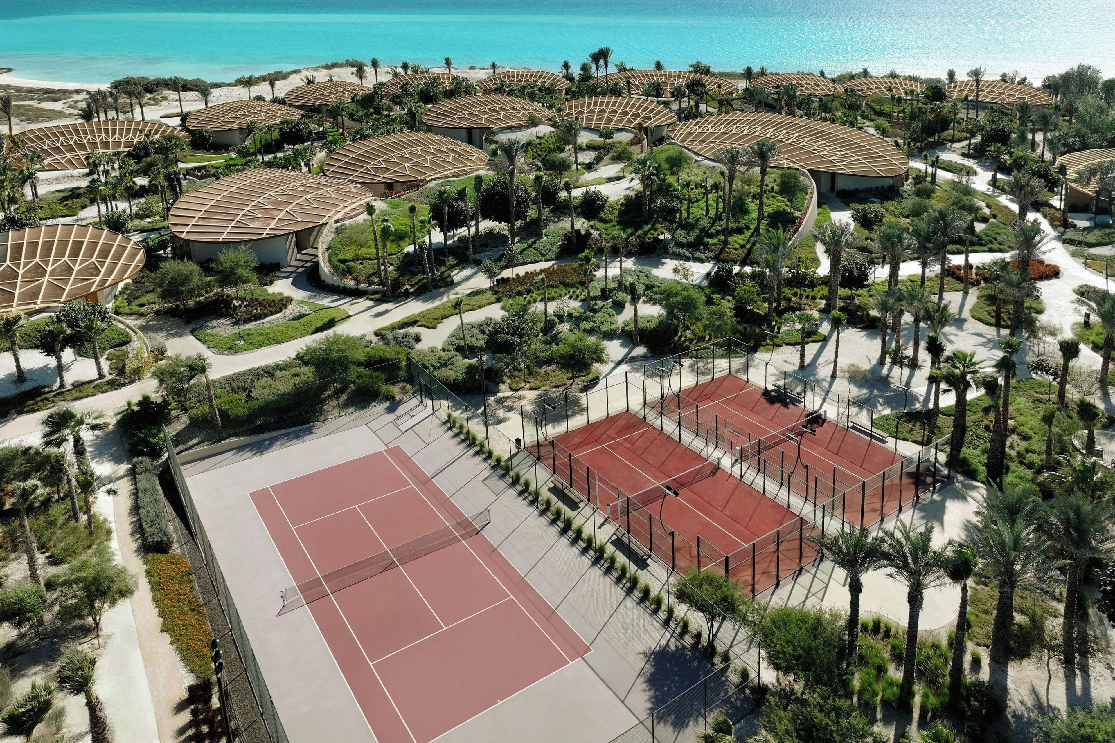 A tennis court surrounded by palm trees and a beach.