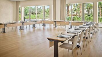 A conference room with long tables, chairs, and large windows with a view of greenery.