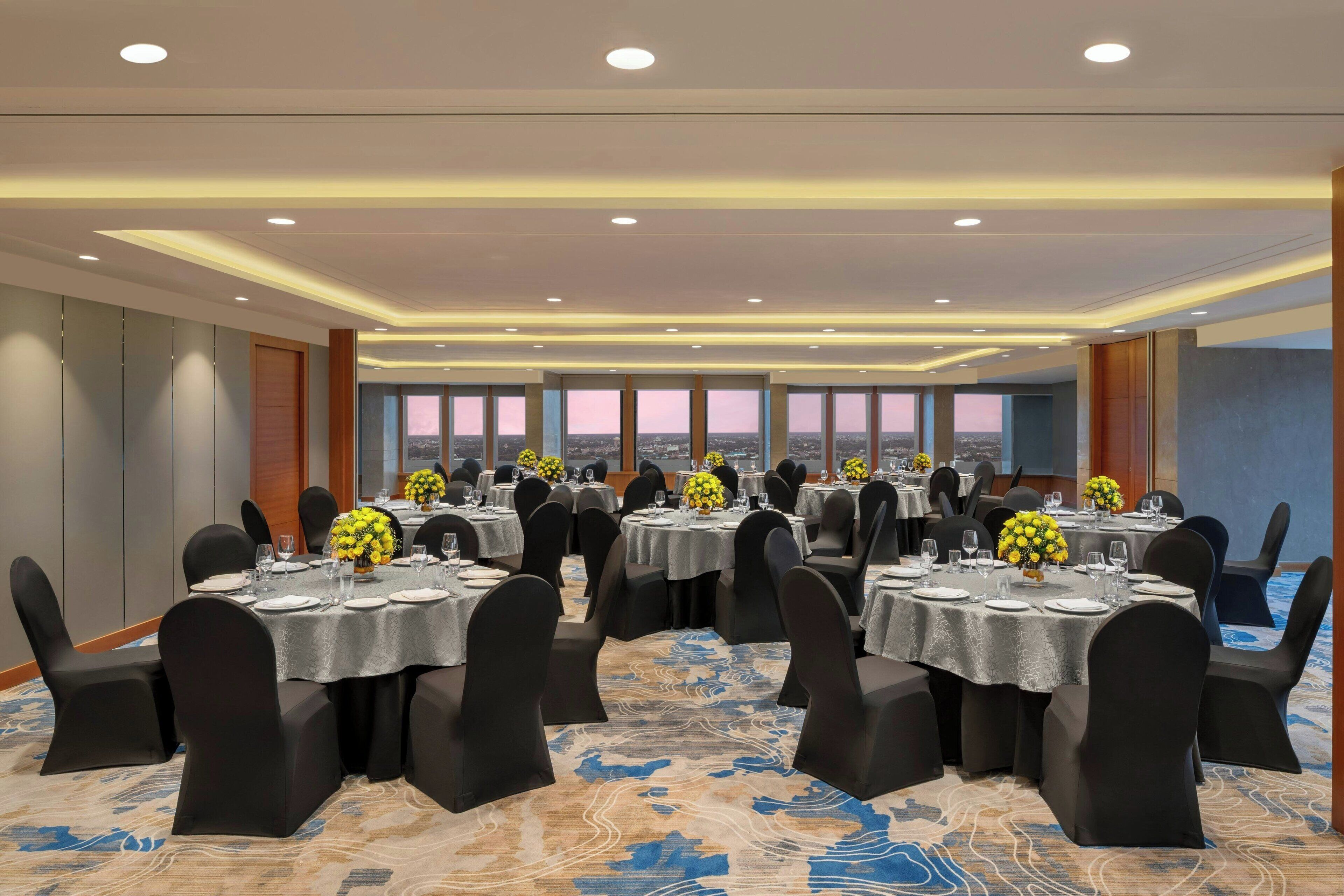 A conference room with multiple tables, black chairs, and floral centerpieces.