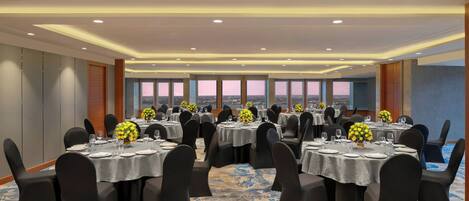 A conference room with multiple tables, black chairs, and floral centerpieces.