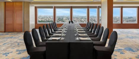 Un salón de conferencias con una larga mesa, sillas negras y ventanas amplias con vistas a la ciudad.
