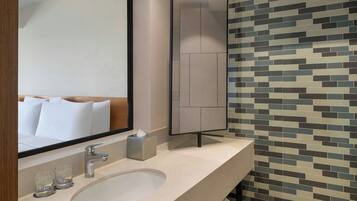 A modern bathroom with a large mirror, a sink, two glasses, a towel, and a tiled wall.