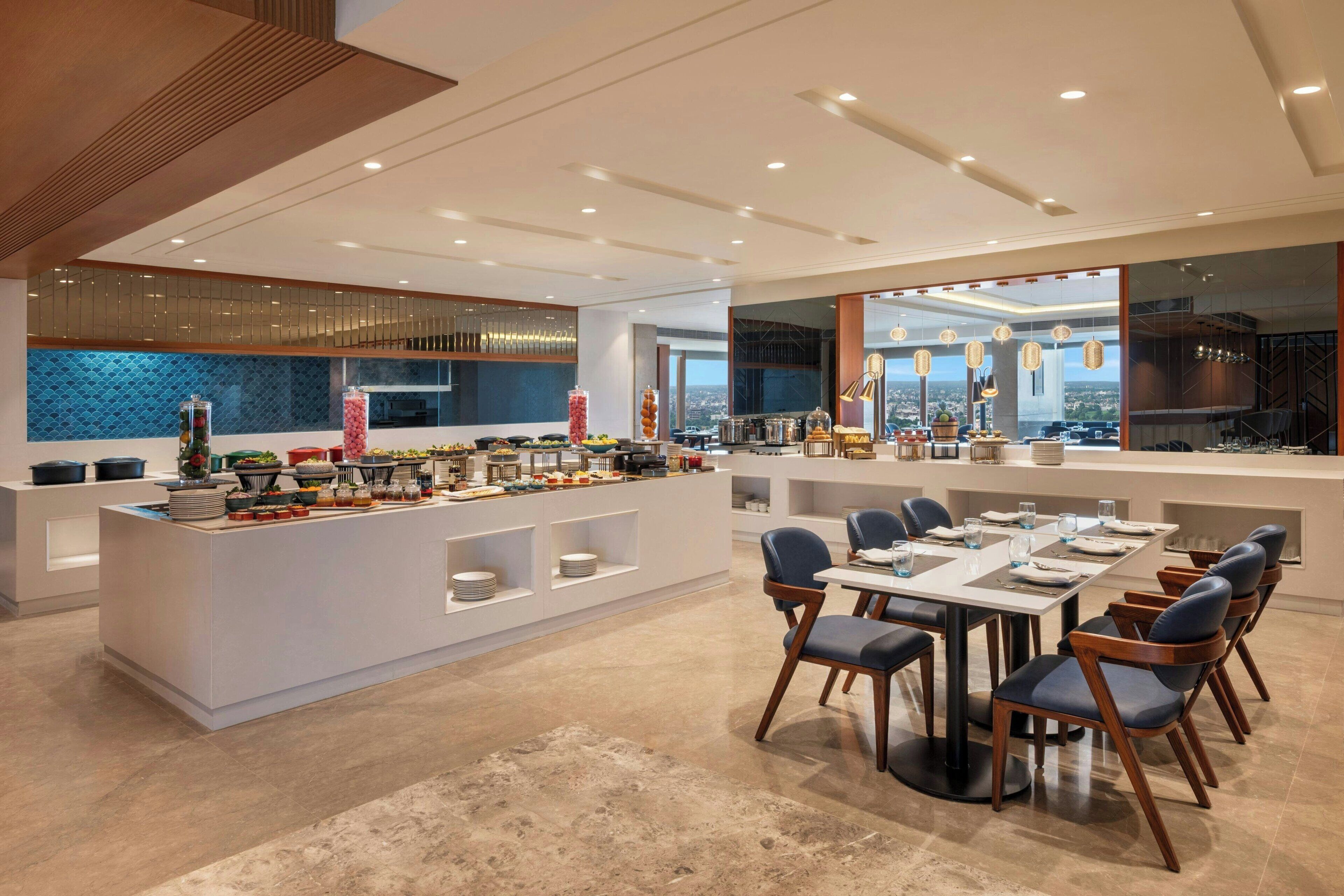 A modern dining area with a central island, multiple seating arrangements, and a view of the cityscape through large windows.
