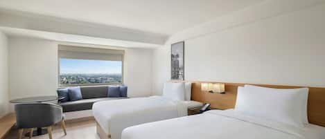 A hotel room with two beds, a sofa, a small table, and a window with a city view.