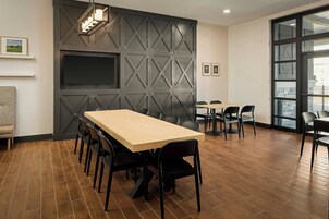 Una sala de conferencias con una larga mesa, sillas, una pantalla de televisión y un ventanal grande.