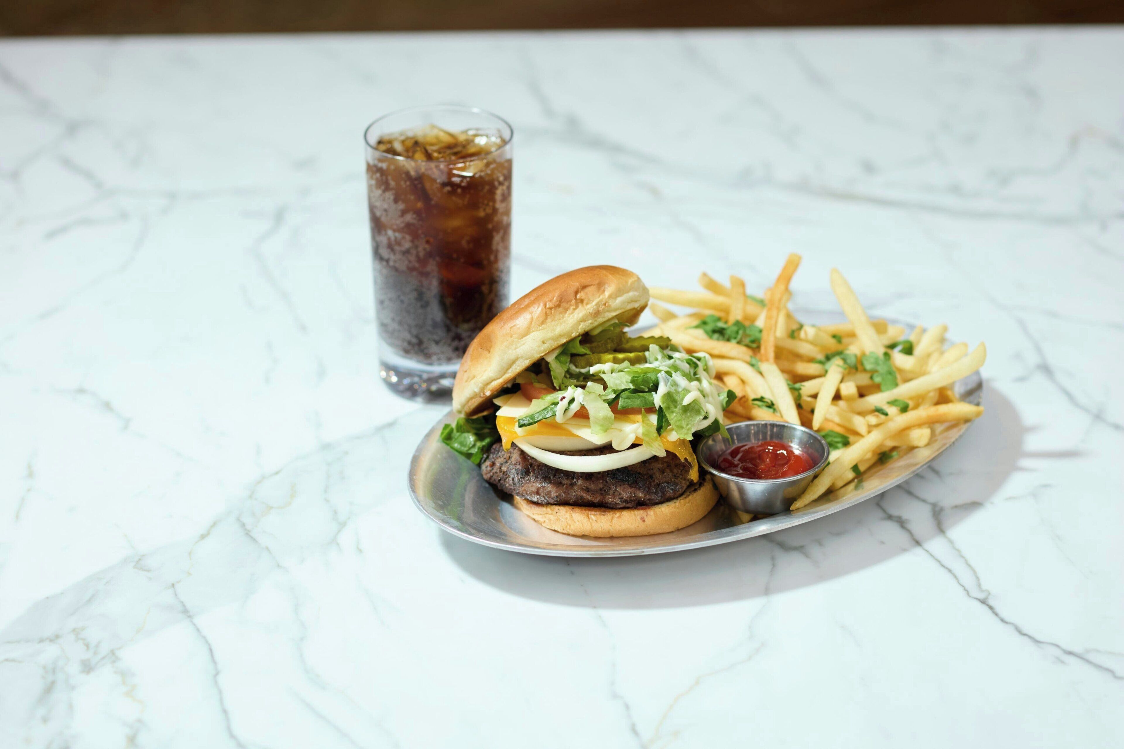 A meal consisting of a burger, fries, and a drink on a marble surface.