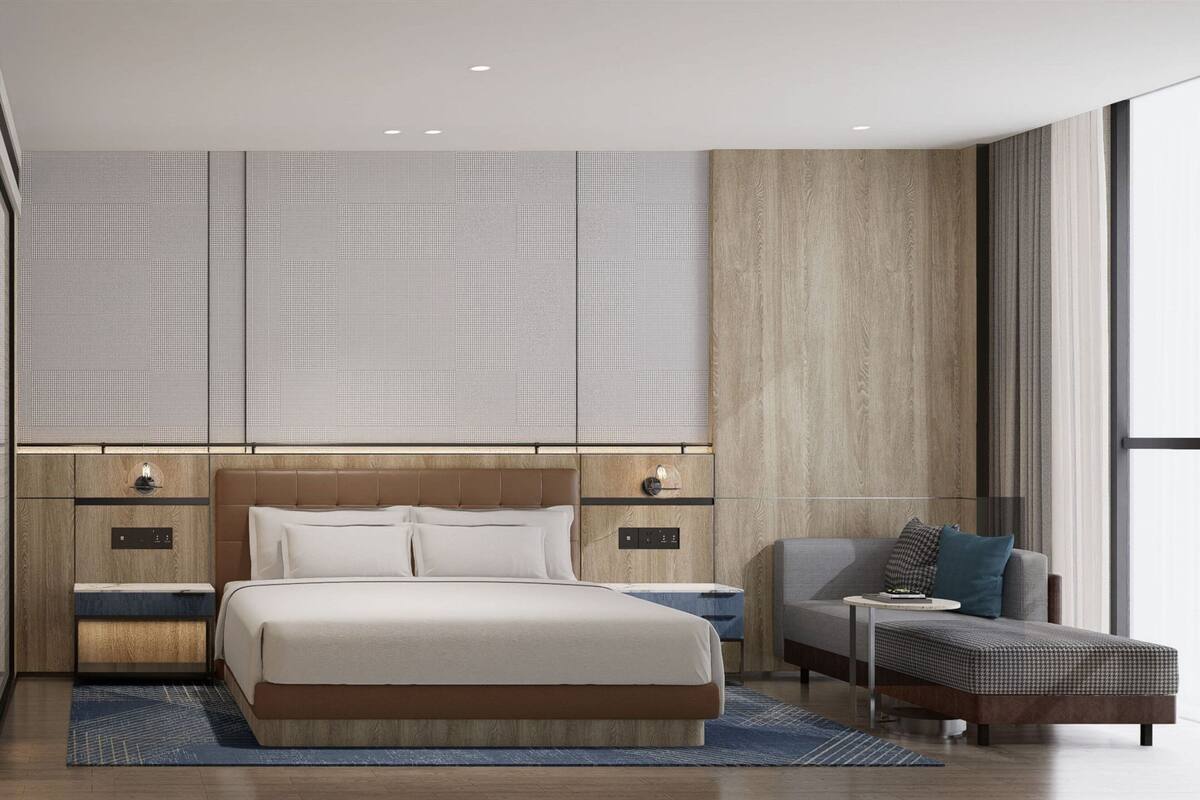 A modern hotel room with a large bed, a sofa, a small table, and a view of the city through large windows.