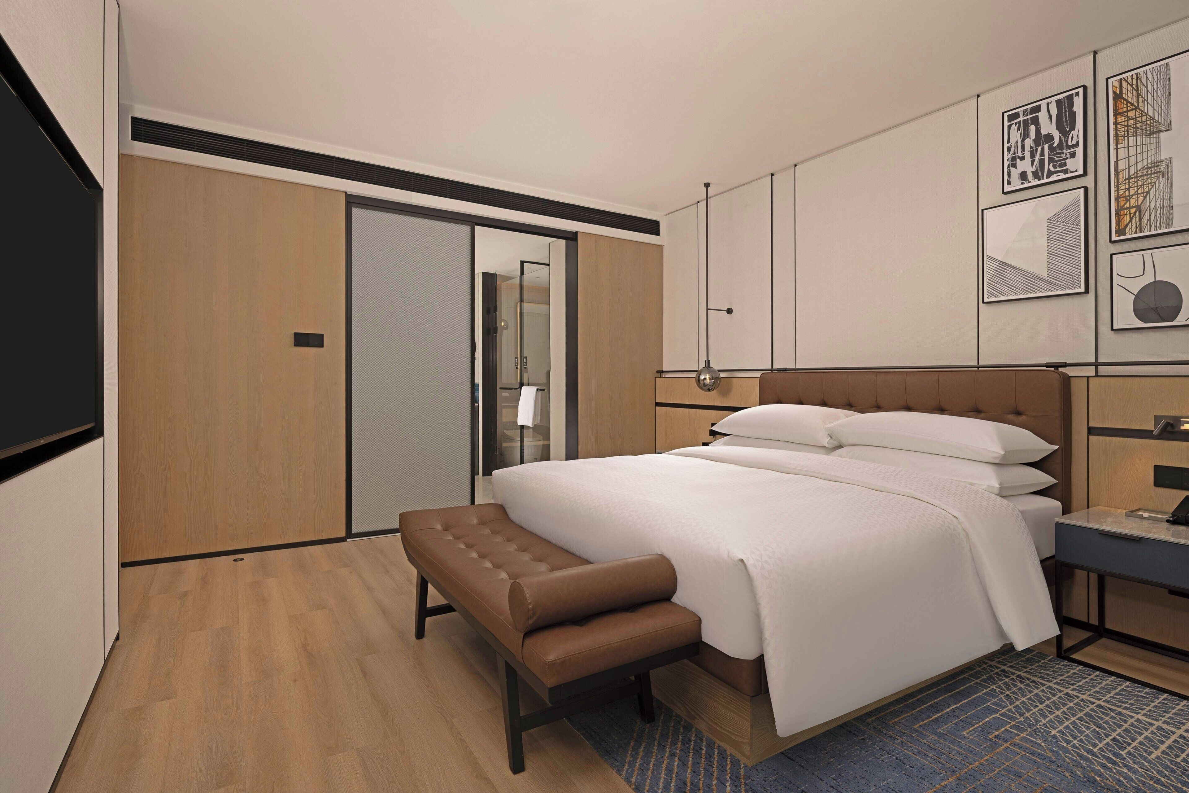 A modern hotel room with a large bed, a bench, a desk, and a wardrobe.