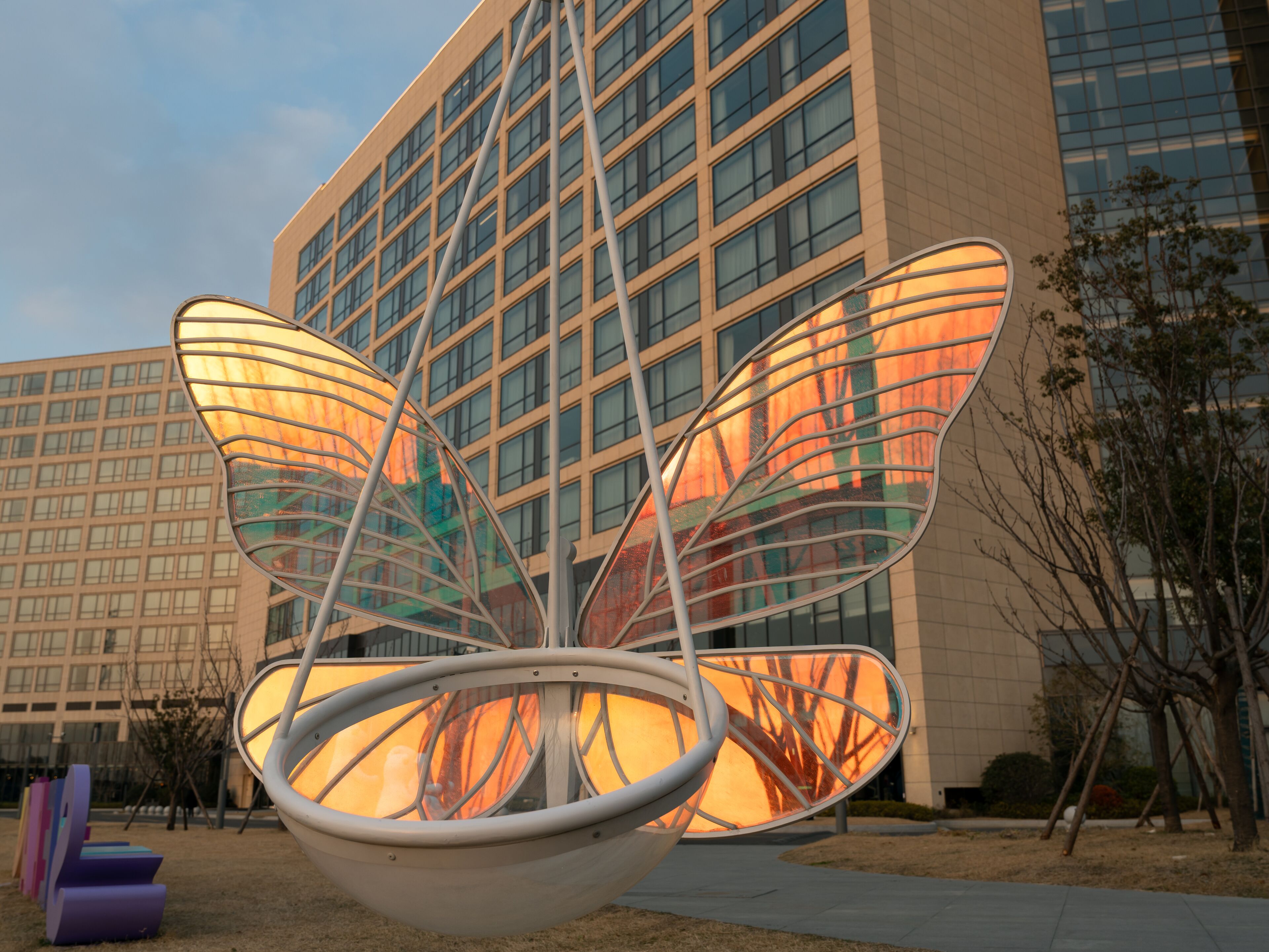 A modern building with a large glass facade and a unique metallic sculpture in front.