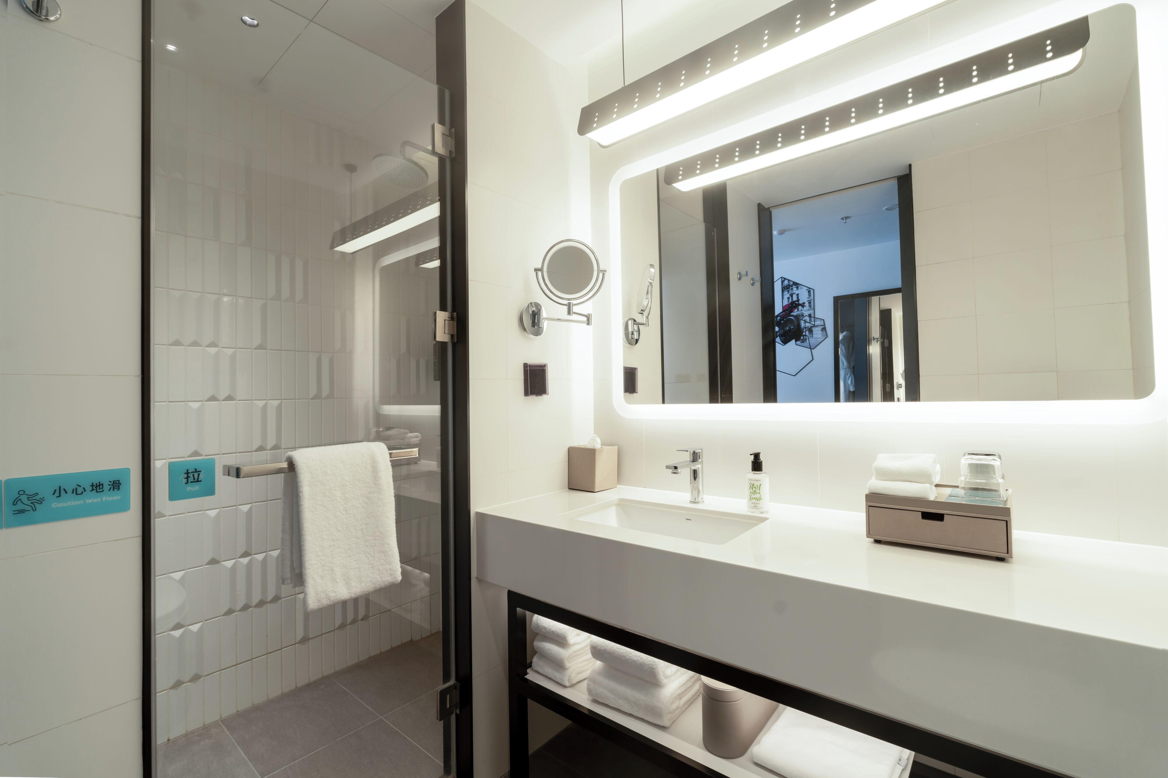 Un baño moderno con cabina de ducha de vidrio, un lavamanos blanco con espejo y un perchero para toallas.
