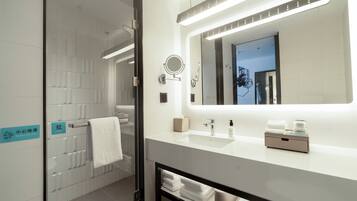 Un baño moderno con cabina de ducha de vidrio, un lavamanos blanco con espejo y un perchero para toallas.