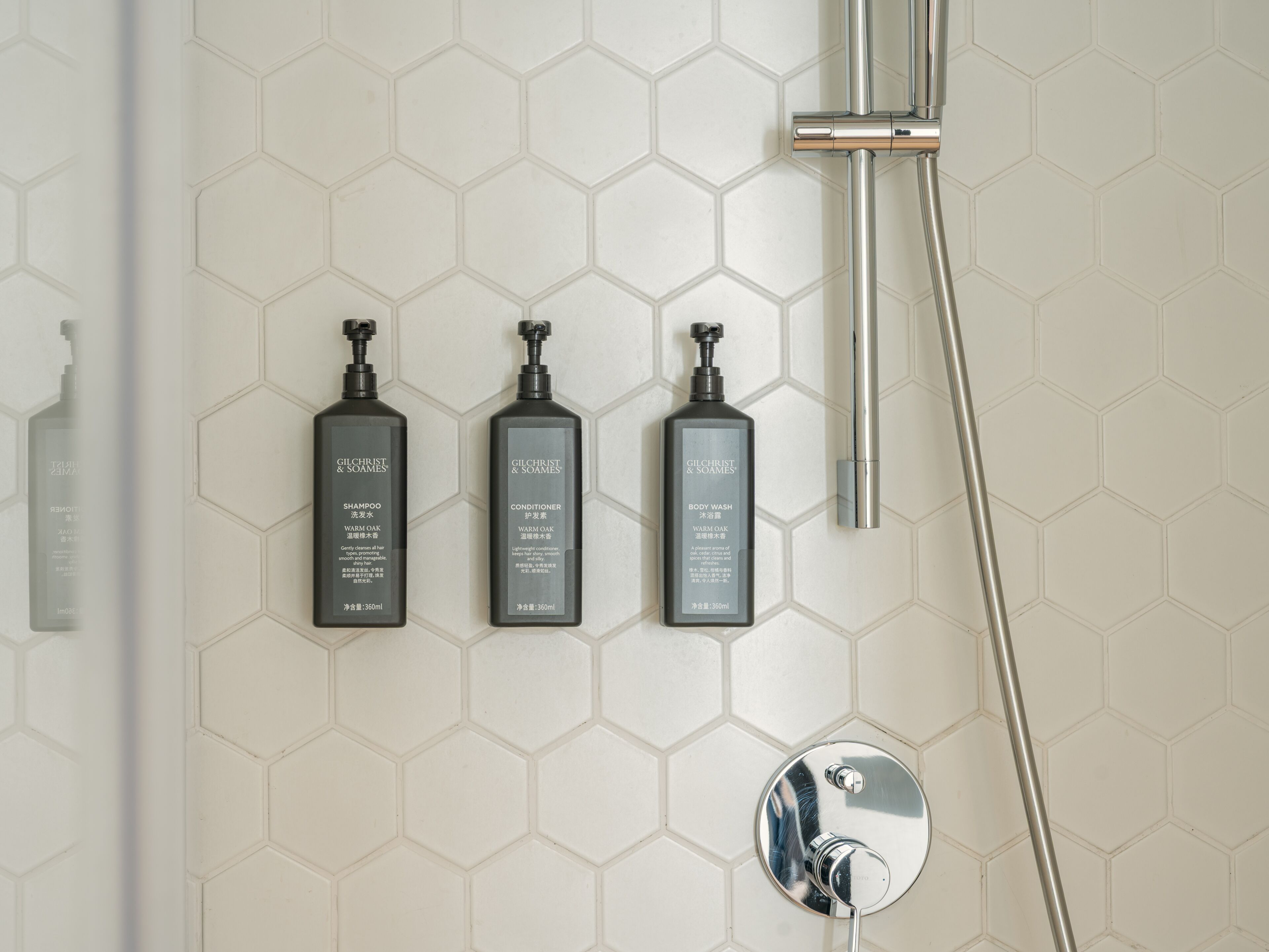 A bathroom with a shower, three Gilchrist & Soames products, and a hexagonal tiled wall.