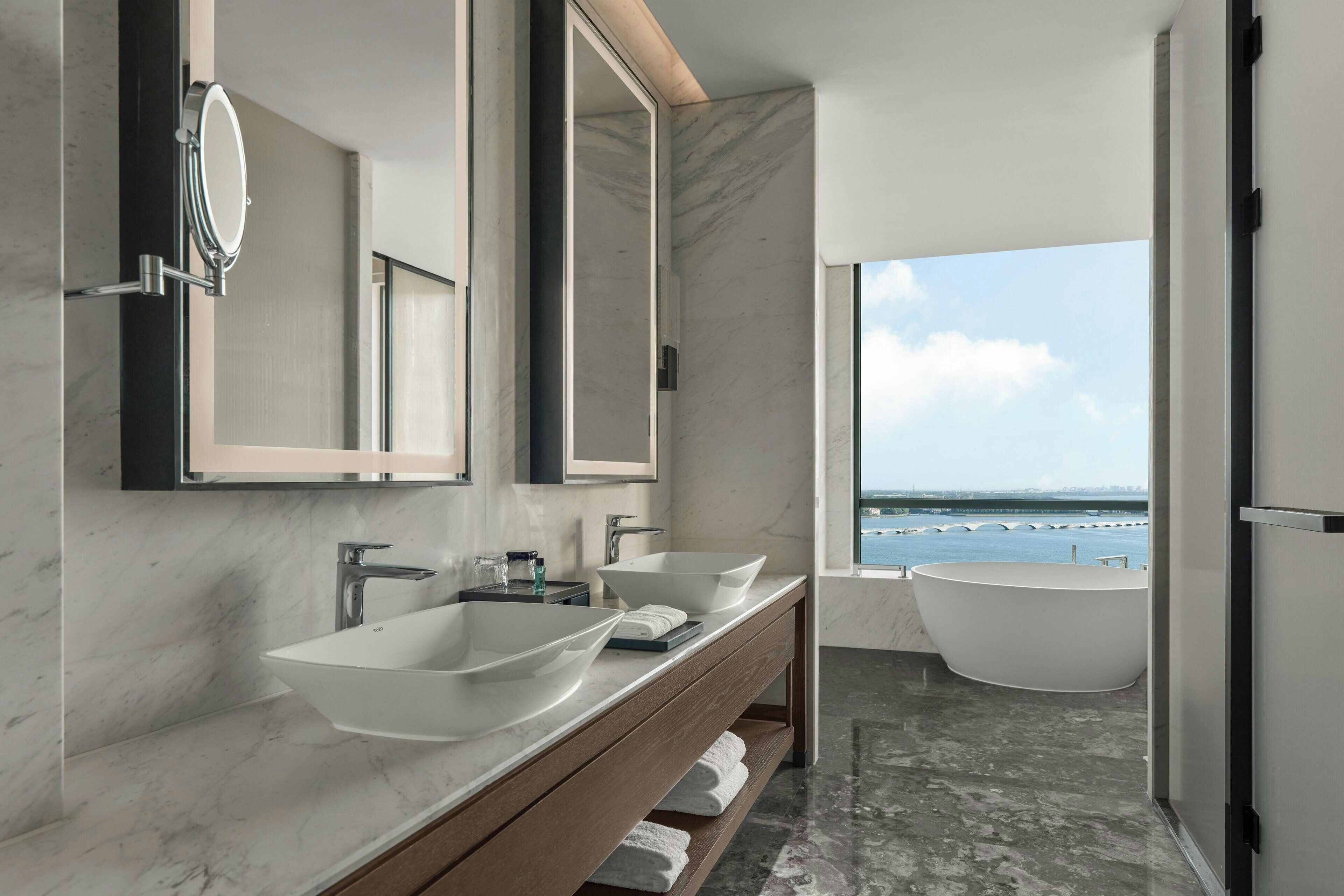 A modern bathroom with two sinks, a large mirror, and a freestanding bathtub.