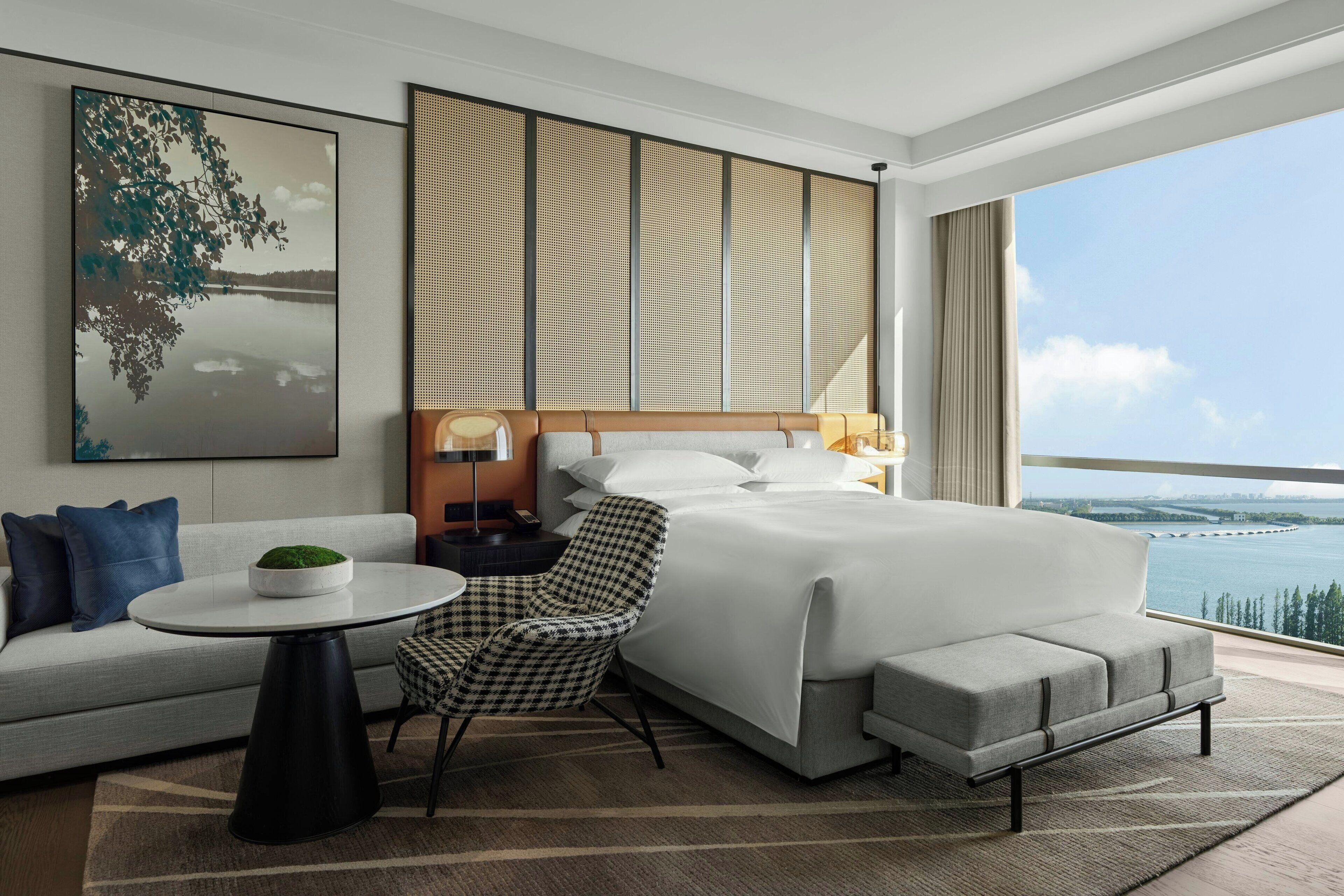 Camera d'albergo moderna con un letto grande, una poltrona, un tavolino e vista su un corpo d'acqua.