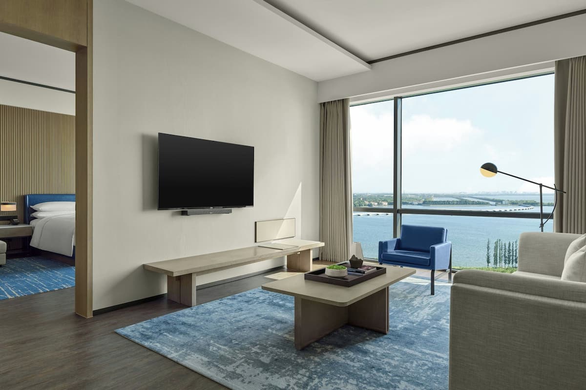 Een moderne hotelkamer met een grote televisie, een bureau, een comfortabele bank en uitzicht op het water.