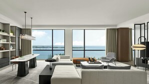 A modern living room with a large window overlooking a body of water, a sofa, a coffee table, and a dining area with a table and chairs. - Sheraton Kunshan Dianshan Lake (Suzhou)