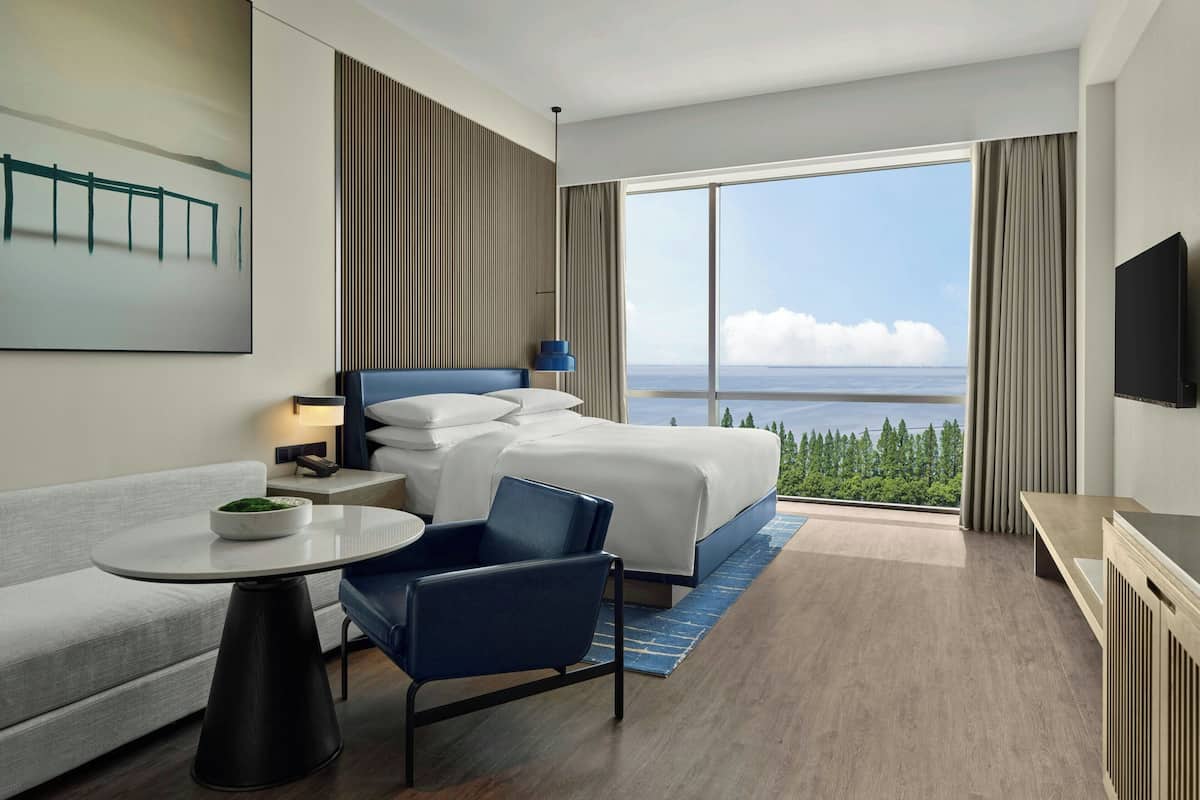 Een moderne hotelkamer met een groot bed, een zithoek met een tafel en uitzicht op zee.